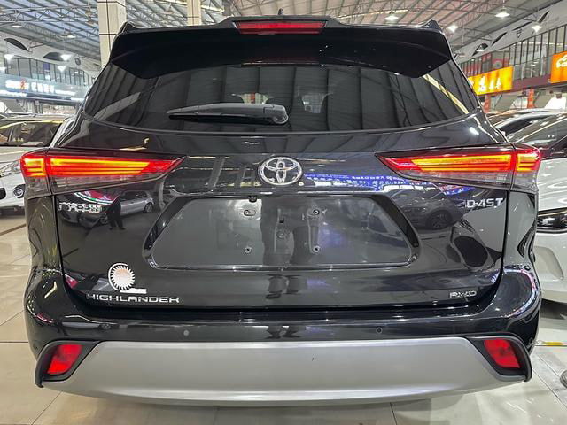 Вид сзади Toyota Highlander (сентябрь 2022): крышка багажника, задние фонари, эмблема Toyota и элементы бампера в выставочном зале.