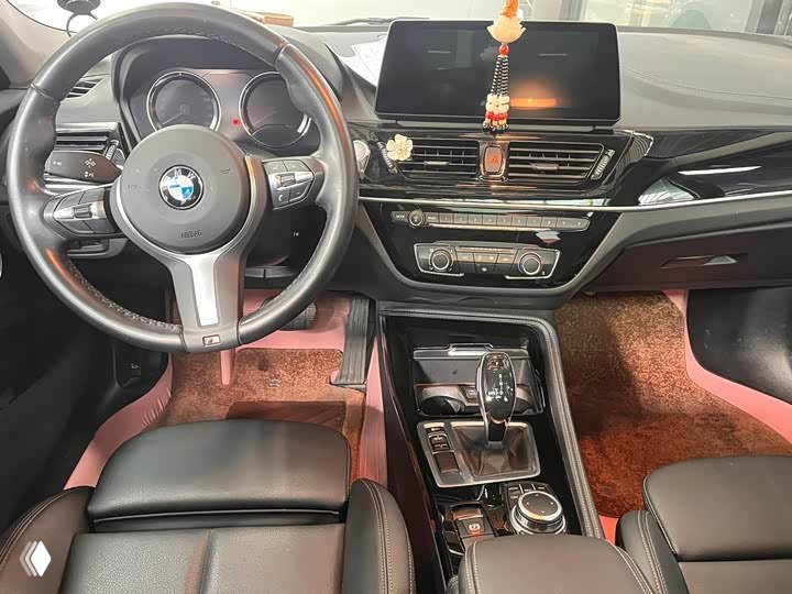 Интерьер BMW 1 Series 120i M Sport: руль с логотипом BMW, мультимедийный экран и центральная консоль с селектором АКПП, чёрная отделка сидений.