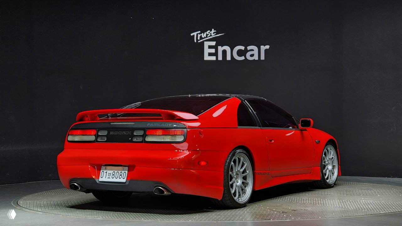 Задняя трёхчетвертная проекция красного Nissan 300ZX Z32 со спойлером и двумя выхлопными патрубками на студийном фоне с надписью Encar.