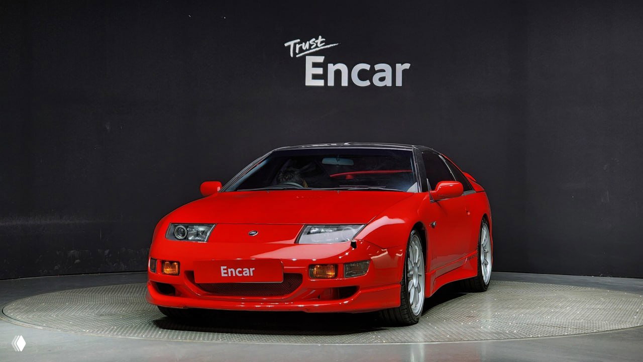 Красный Nissan 300ZX Z32 в анфас в студийной съёмке, чёрный потолок и эмблема Encar на стене — акцент на передней части и фарах.