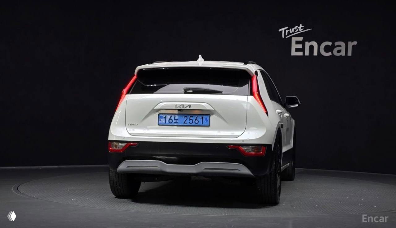 Крупный план задней части белого Kia Niro в студии: геометрия багажника, стоп-сигналы и номерный знак на фоне логотипа Encar.