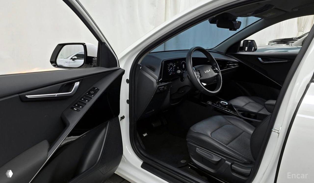 Отрытая передняя дверь и водительское сиденье белого Kia Niro: вид на дверную карту, сиденье и панель управления в салоне автомобиля.