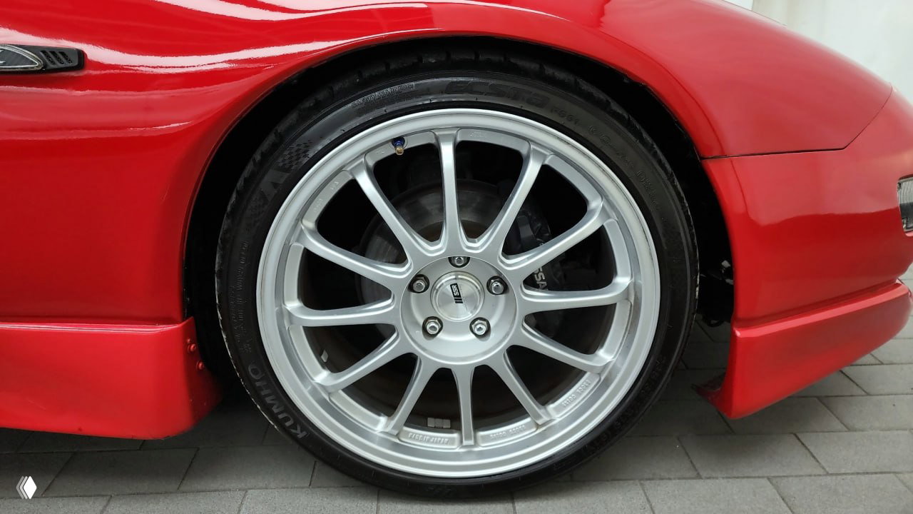 Крупный план легкосплавного диска и шины на красном Nissan 300ZX Z32 — видно состояние колеса и тормозной суппорт, ракурс снизу.