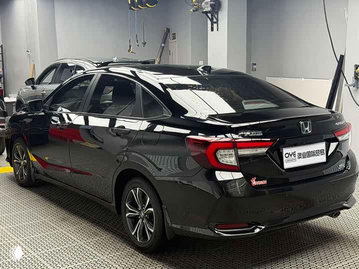 Задний трёхчетвертной вид Honda Crider 2021 в чёрном цвете: багажник, фонари и задняя часть кузова в дилерском гараже с другим автомобилем на заднем плане.