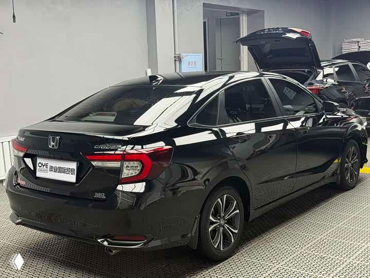 Боковой вид сзади Honda Crider 2021: чёрный кузов, колёсные диски, отражения освещения и открытый багажник у соседней машины в сервисе.