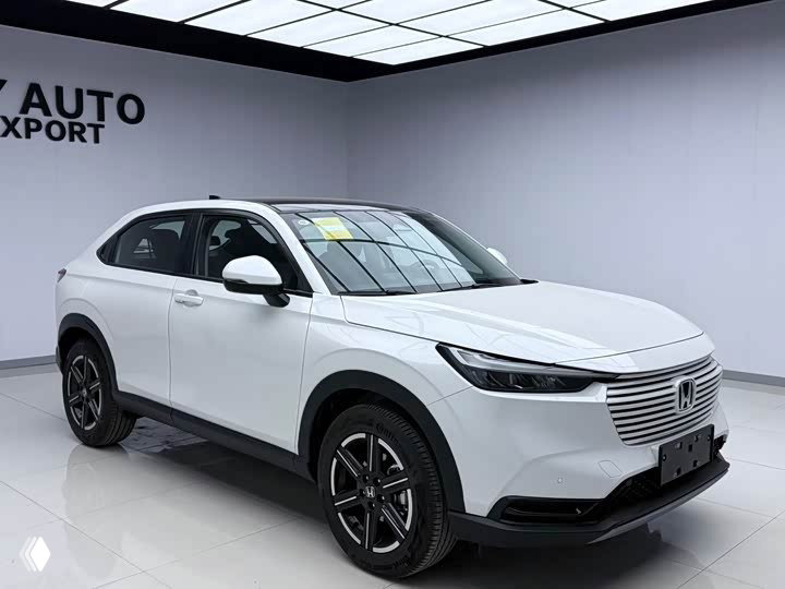 Белый Honda Vezel 2023, боковой ракурс в выставочном помещении, видны диски и профиль автомобиля на белом фоне.