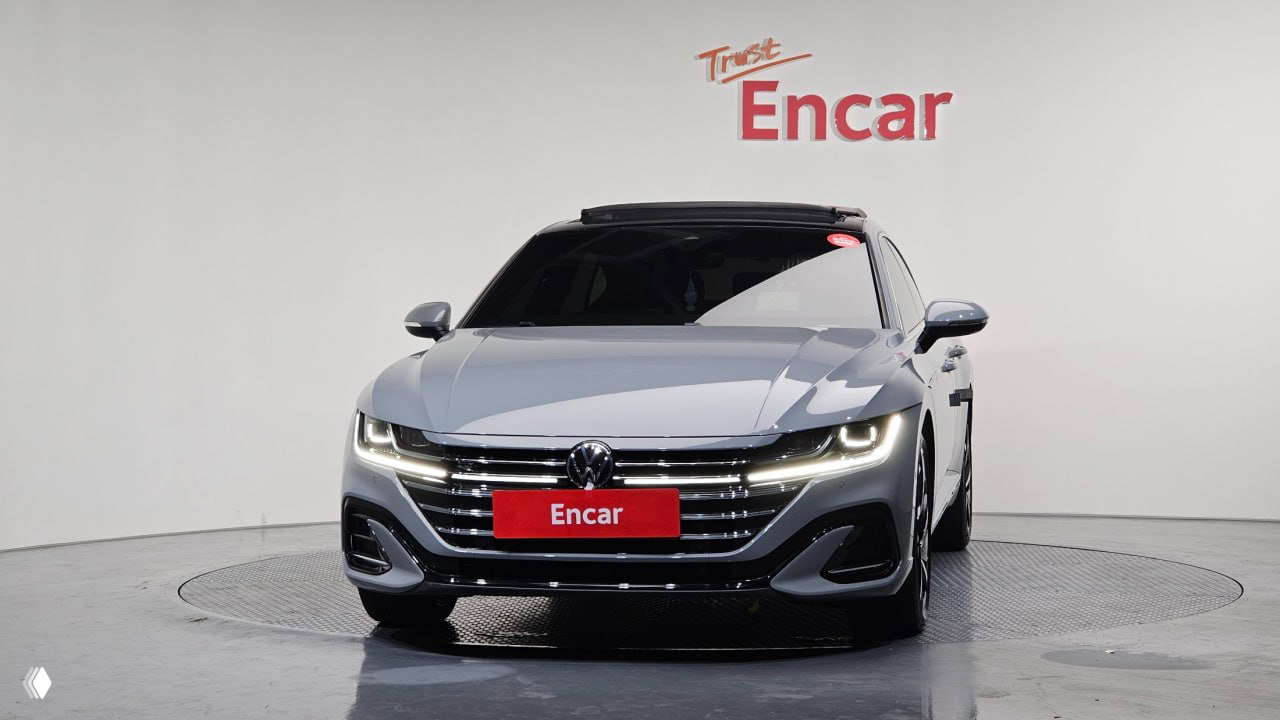 Анфас: Volkswagen Arteon 2022 в шоуруме Encar — заметны фирменная эмблема VW, хромированная решётка и дневные ходовые огни автомобиля.