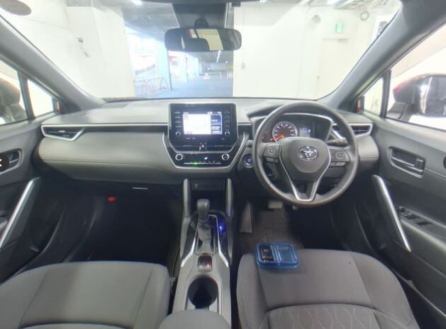 Панель приборов и центральная консоль Toyota Corolla Cross, руль справа, мультимедийный экран, селектор и передние сиденья крупным планом в ангаре.