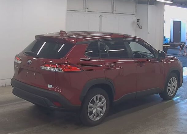 Задний три четверти ракурс красной Toyota Corolla Cross в ангаре, видны багажник, задние фонари, бампер и общий профиль автомобиля без автономеров.