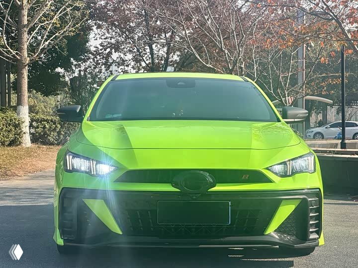 Фронтальный вид ярко‑зелёного GAC Leopard: включённые фары, заметна решётка радиатора и агрессивный передний бампер на фоне городского пейзажа.