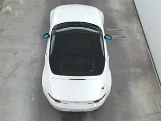 Вид сверху на белую Mazda Roadster с закрытым чёрным мягким верхом, видна общая пропорция кузова и состояние лакокрасочного покрытия.