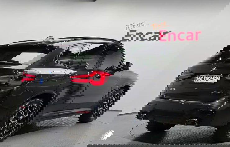 Задняя часть чёрного BMW X3 M Sport 2023 года на белом фоне, видна задняя оптика, выхлопные патрубки и багажная дверь.