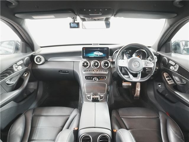 Фото салона Mercedes C‑Class 2019: панель приборов, мультимедиа-экран, рулевое колесо, центральный туннель и кожаные сиденья — вид спереди.