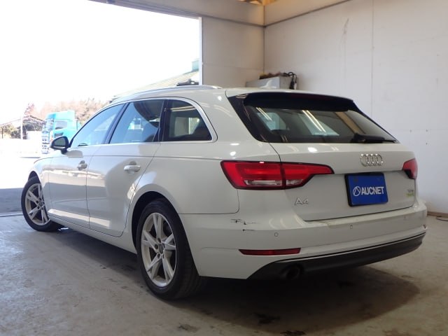 Вид сзади на белый Audi A4 2018 (универсал) в помещении — видны задние фонари, багажник и номер с логотипом AUCNET.