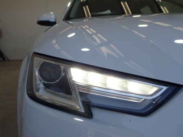 Крупный план передней фары Audi A4 2018 с включенным светодиодным элементом и отражением потолочного освещения в фаре.