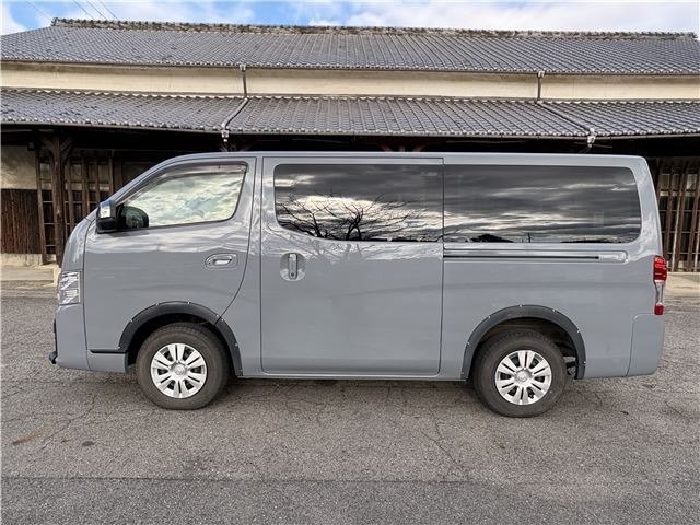 Боковой профиль серого Nissan Caravan 2022 — вид слева, видны колёса, стекла и общий профиль микроавтобуса на открытой парковке.