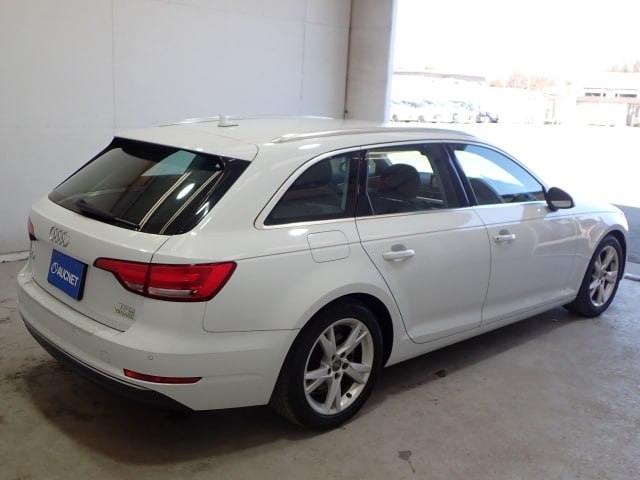Угол сзади‑сбоку белого Audi A4 2018: задние фары, форма крыши и часть багажника, автомобиль на стоянке внутри помещения.