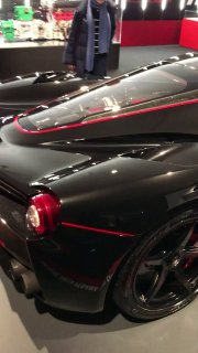 Чёрная спортивная Ferrari крупным планом: кузов, аэродинамические линии и красные акценты на корпусе в выставочном зале.