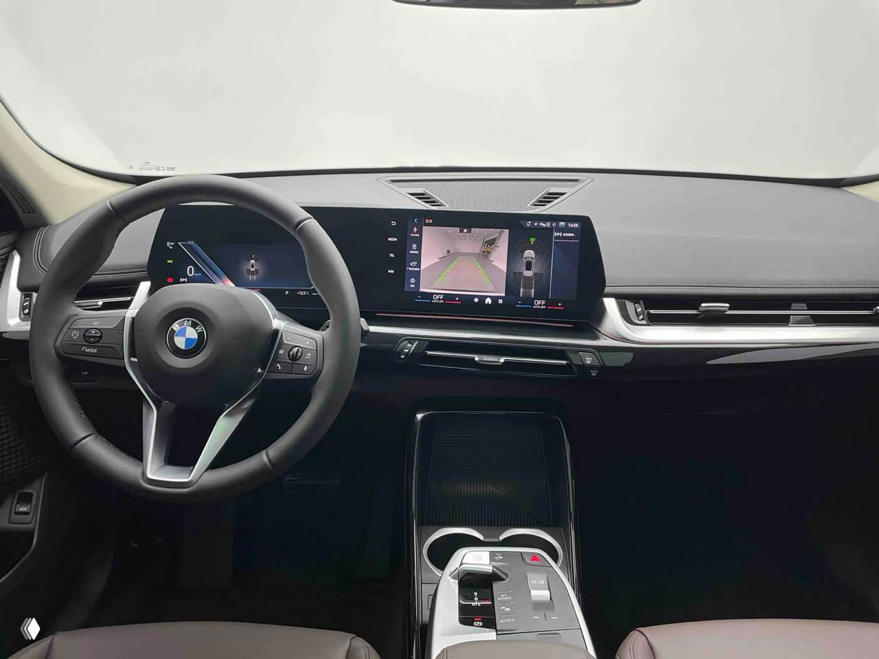 Вид салона BMW X1 с центральной консолью и экраном мультимедиа: руль, большой сенсорный дисплей и посадочная зона водителя.