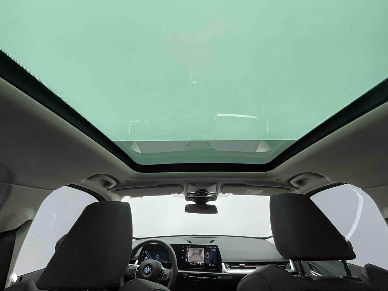 Интерьерный кадр с панорамной крышей BMW X1: вид назад через салон на стеклянный люк и передние кресла, просторный потолочный обзор.