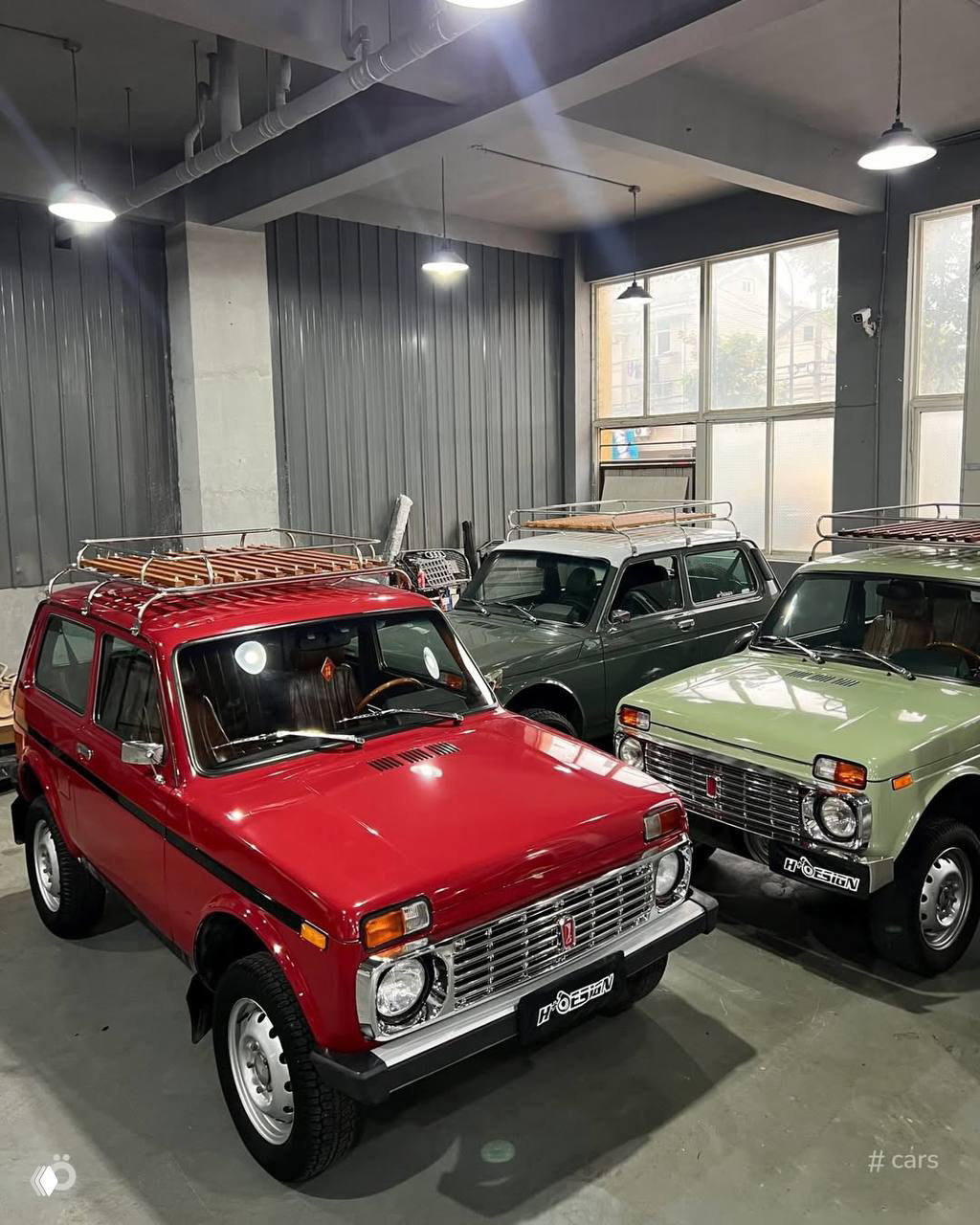 Несколько ретро‑Нив в выставочном зале: красная, зелёная и светлая модели с экспедиционными багажниками на крыше и аккуратным рестайлом.