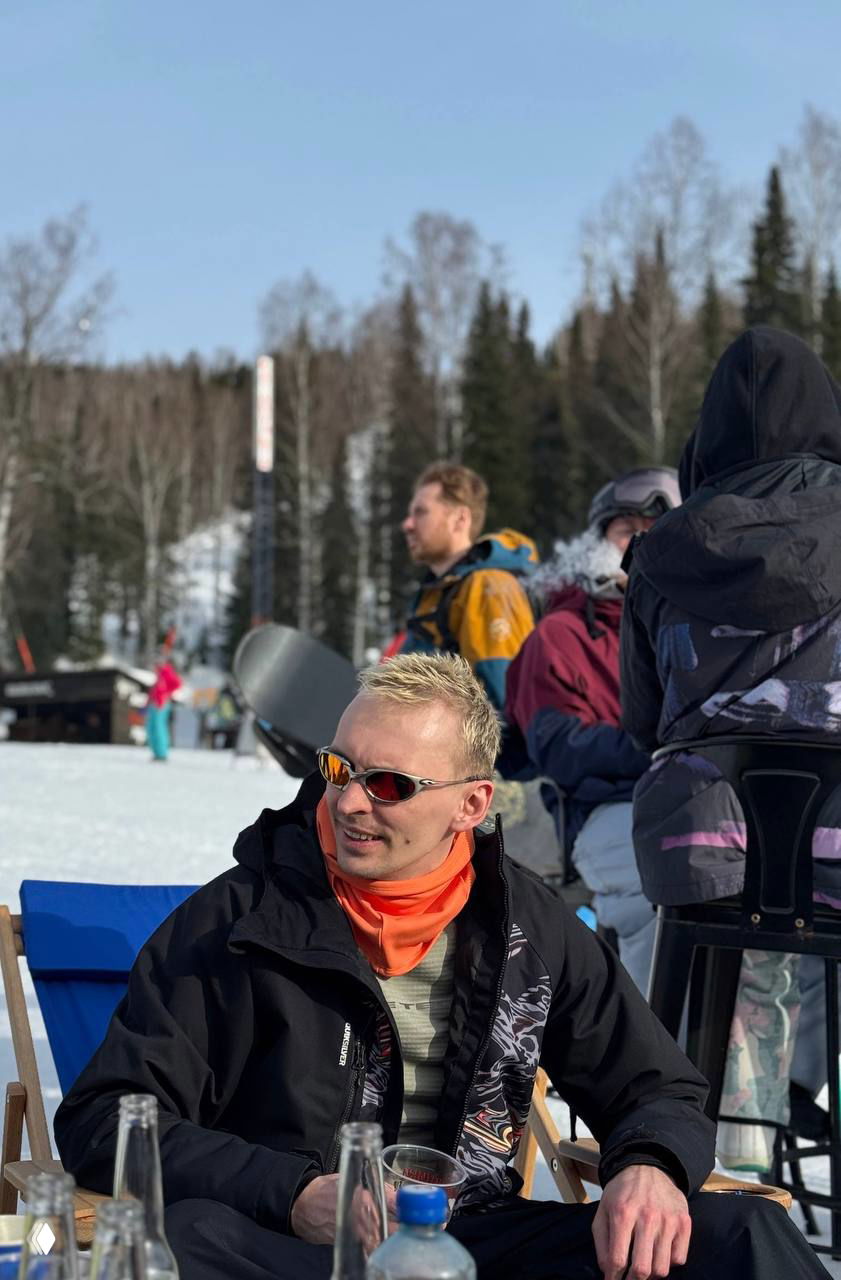 Отдыхающий в солнцезащитных очках на базе курорта, мягкое солнце и весенняя пауза после катания в Шерегеше среди других гостей.
