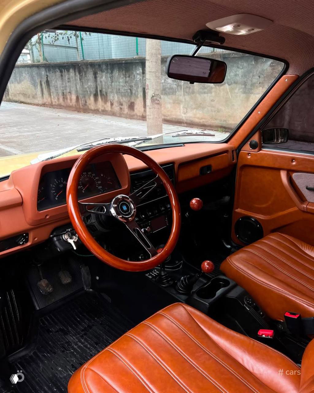 Вид из салона Нивы на кресла с коричневой кожаной обшивкой, деревянный руль и аккуратно оформленная приборная панель в ретро‑стиле.