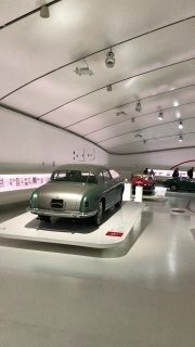 Часть экспозиции Ferrari в музее: ракурс на заднюю часть редкой модели на подиуме в минималистичном белом зале музея.