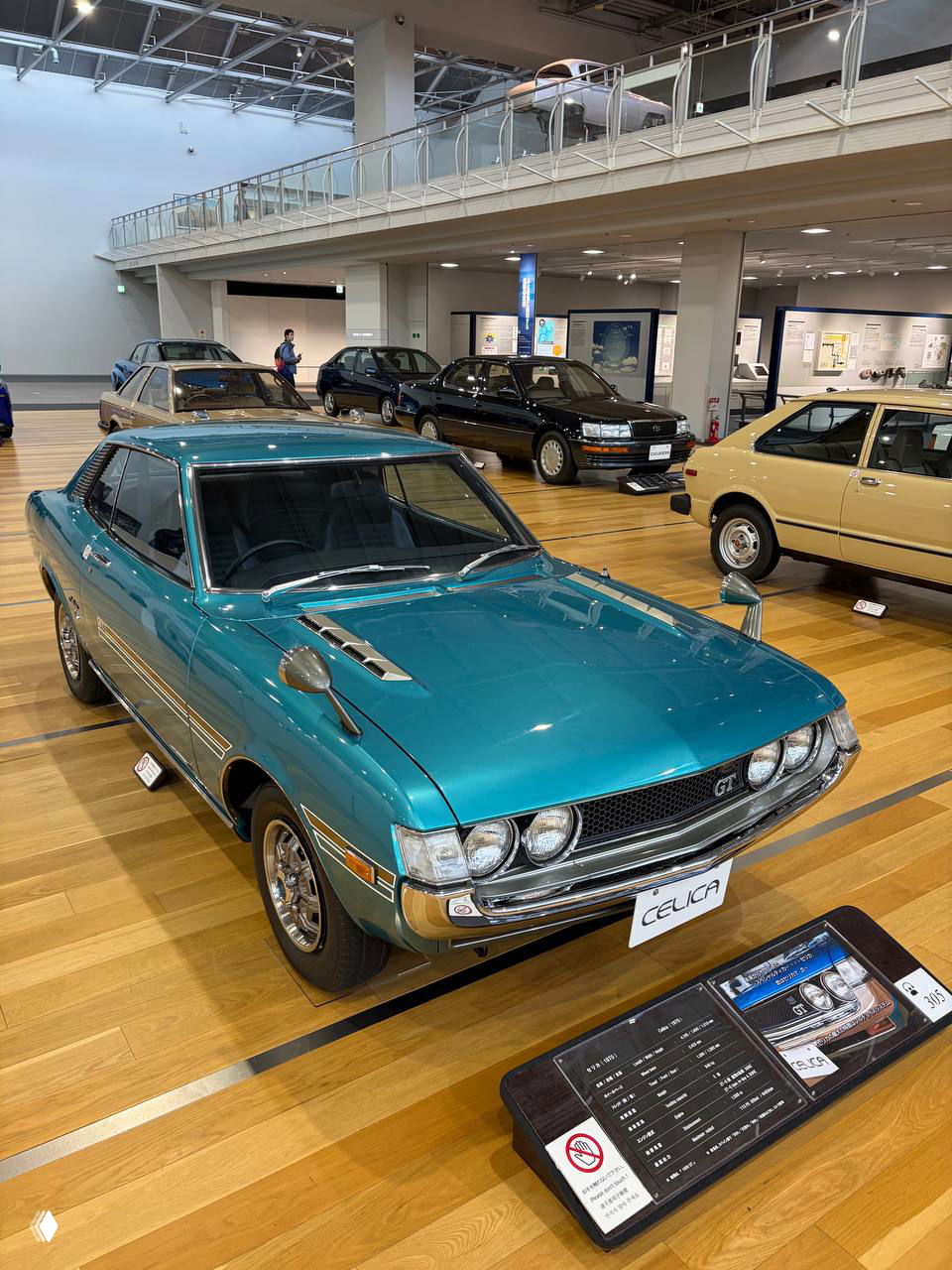 Зал музея с классическими моделями Toyota на деревянном полу: Celica и другие ретро-автомобили, выставленные хронологически для обзора истории бренда.