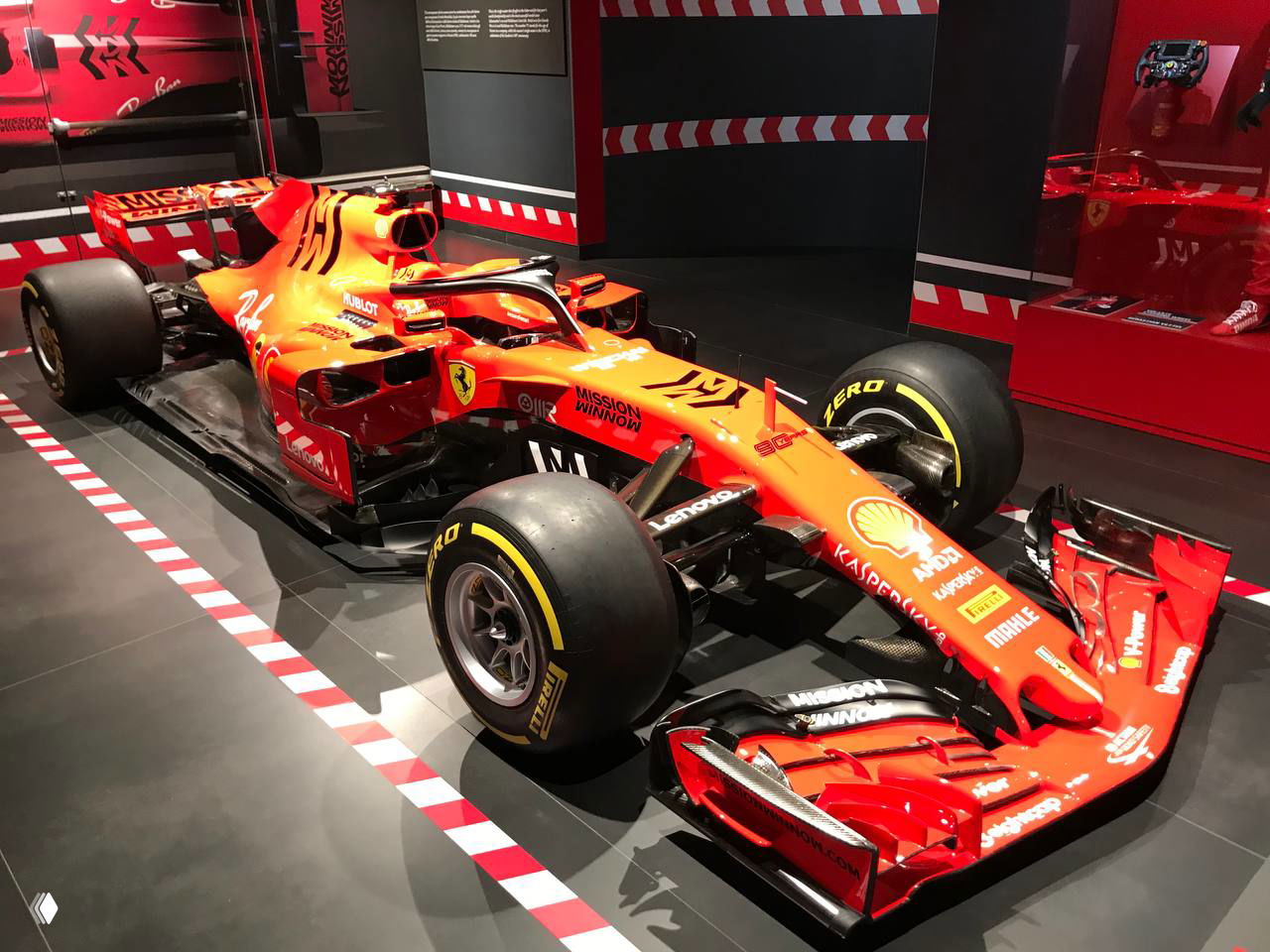 Гоночный болид Ferrari в экспозиции: крупные шины Pirelli, аэродинамические элементы и гоночная графика вокруг подиума.