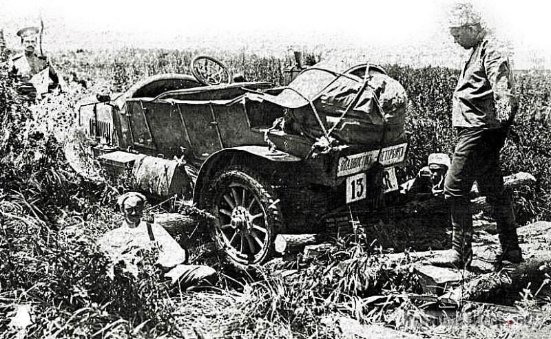 Чёрно-белая фотография повреждённого автомобиля на обочине, мужчина сидит рядом; сцена аварии или поломки в дороге.