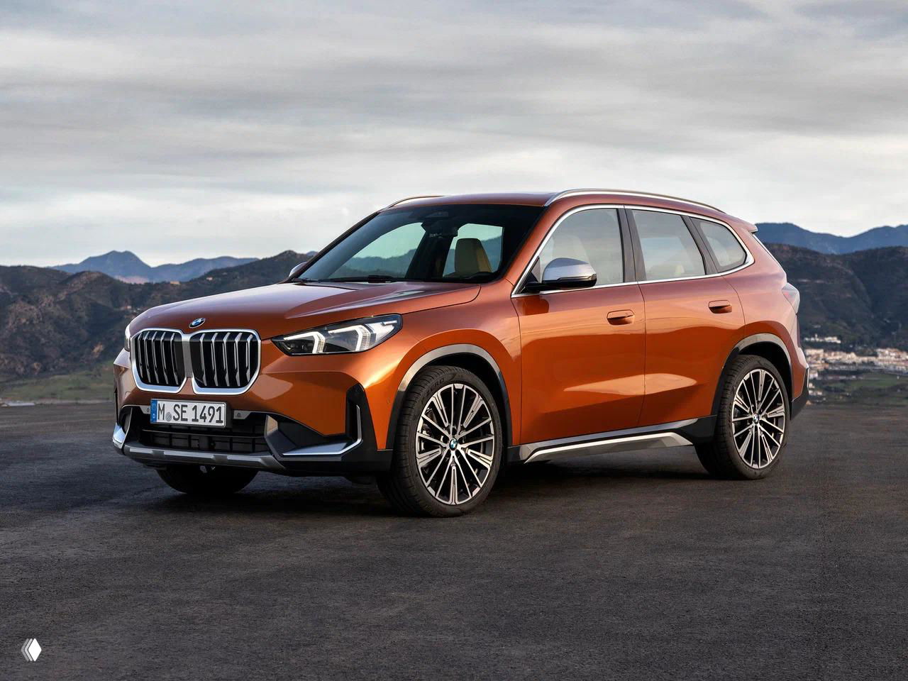 Оранжевый BMW X1 на фоне гор, вид в три четверти подчёркивает компактный SUV-профиль и фирменную решётку радиатора BMW