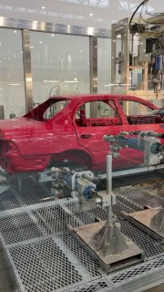 Красный автомобиль в зоне окраски и сборки музея Toyota: манипуляторы и технологическое оборудование демонстрируют этапы производственного процесса.