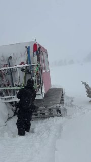 Райдер рядом с ратраком и закреплёнными досками, густой снег и ограниченная видимость в верхней зоне Шерегеша во время поездки.