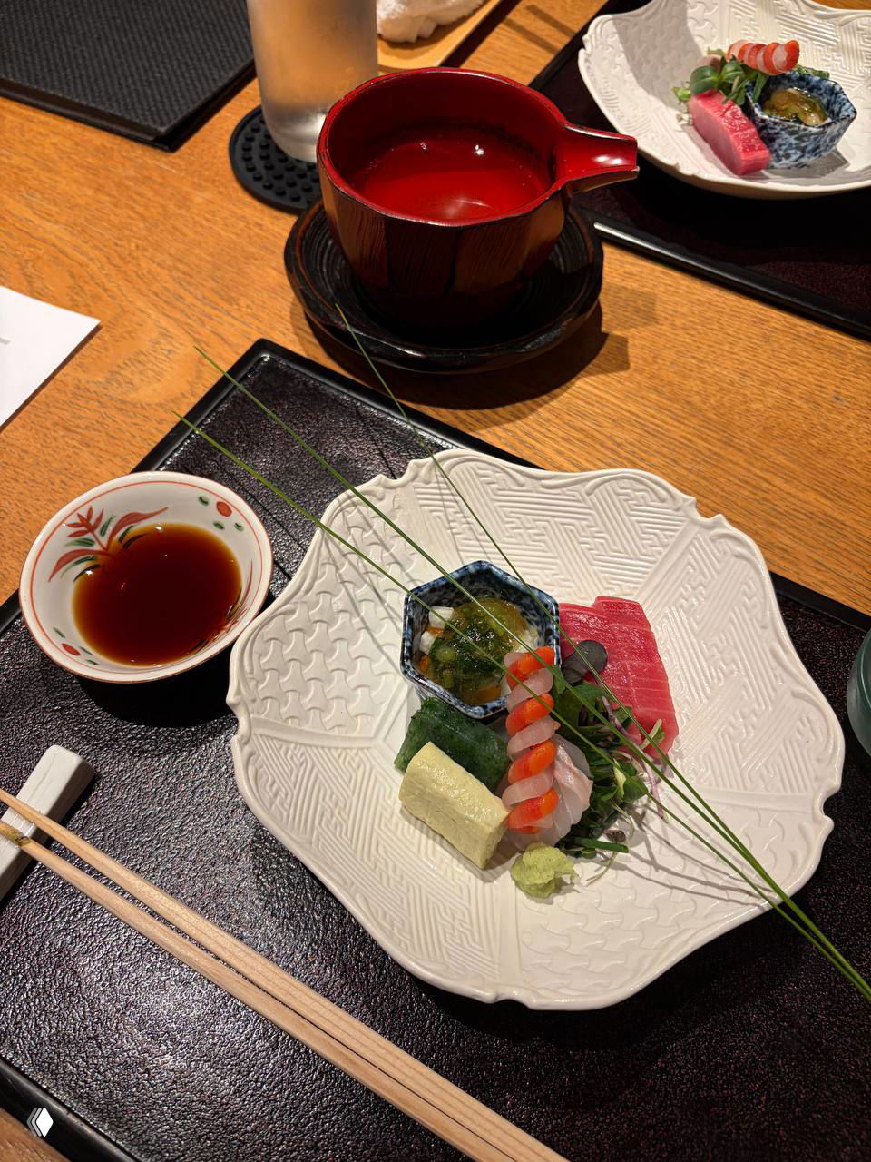Белая тарелка с ассорти из сашими и роллов, соевый соус в маленькой пиале и палочки на подставке — минималистичная сервировка.