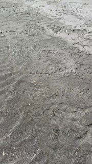 Чёрный вулканический песок вблизи, рисунки от воды и ветра, текстура побережья Камчатки в макро-кадре.