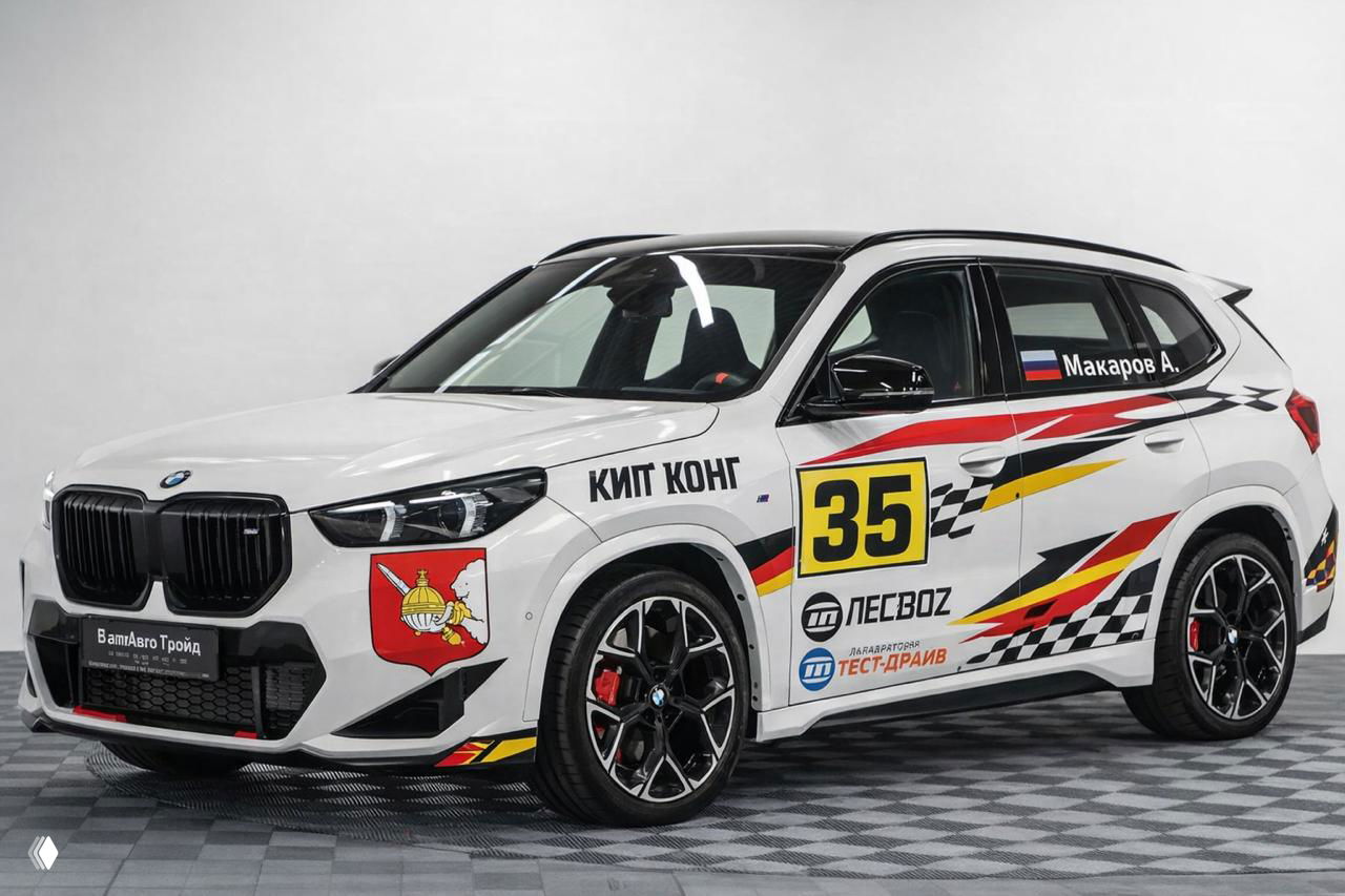 Белый BMW X2 с крупным номером 35 и множеством спонсорских логотипов на дверях и крыльях, вид сбоку в студии