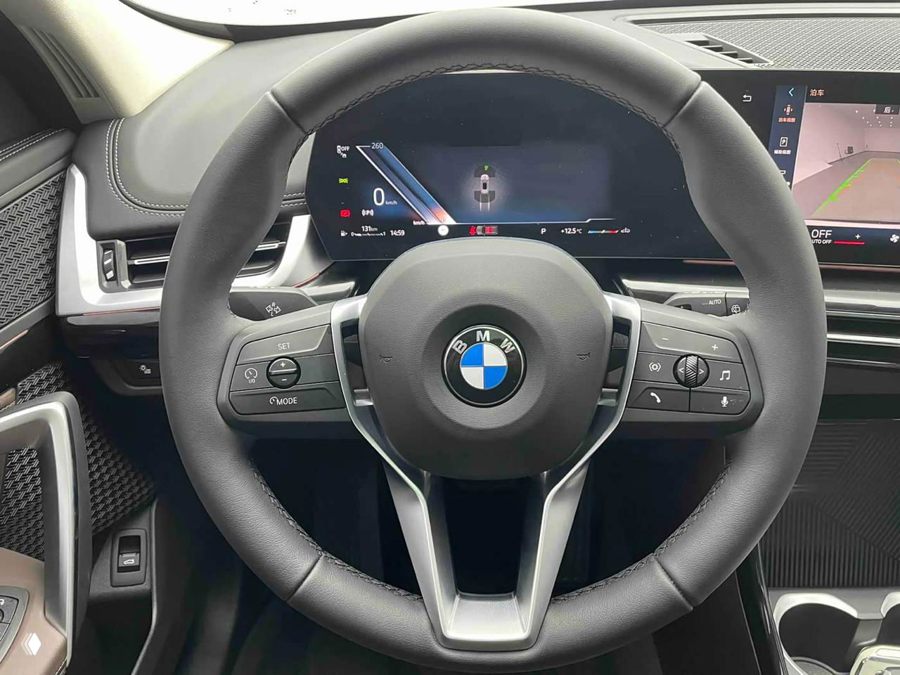 Крупный план рулевого колеса BMW с эмблемой, вид на цифровую приборную панель и элементы управления на руле — интерьерный снимок.