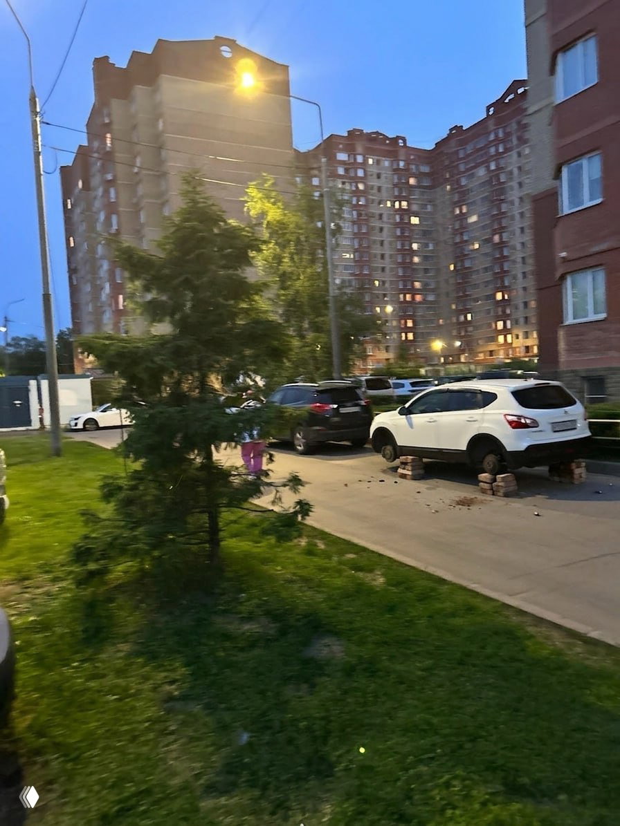 Автомобиль без колёс, поставлен на кирпичи во дворе, возле многоквартирного дома вечером — имитация кражи колёс для розыгрыша в промте.