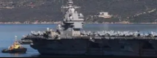 Авианосец и буксир у берега: крупный военный корабль в порту, иллюстрация к новости о военно‑морской активности и ремонте.