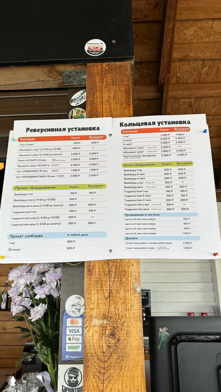 Фотография прайс-листа и информации об услугах вэйк-парка, прикреплённая на деревянной стойке ресепшена.