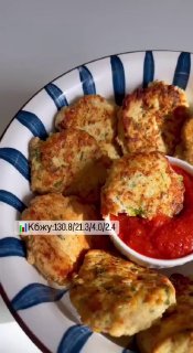 Тарелка с золотистыми куриными оладьями с зеленью, рядом соус томатного цвета; вид сверху, домашняя подача блюда.