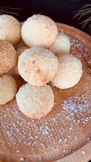 Круглые кокосовые сырники на деревянной тарелке, обвалянные в кокосовой стружке, домашняя выпечка в тёплых тонах