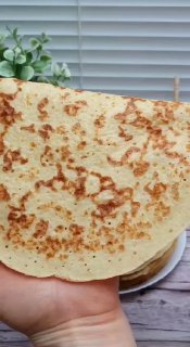 Крупный план одного готового творожного ПП‑блина на ладони с румяной золотистой корочкой; на фоне видна тарелка и жалюзи