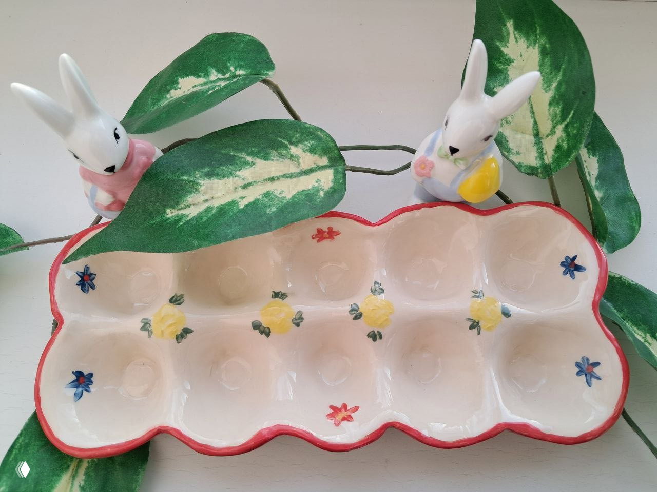 Росписная керамическая подставка для яиц с жёлтыми цветами и красной окантовкой, на фоне декоративных листьев и фарфоровых зайцев