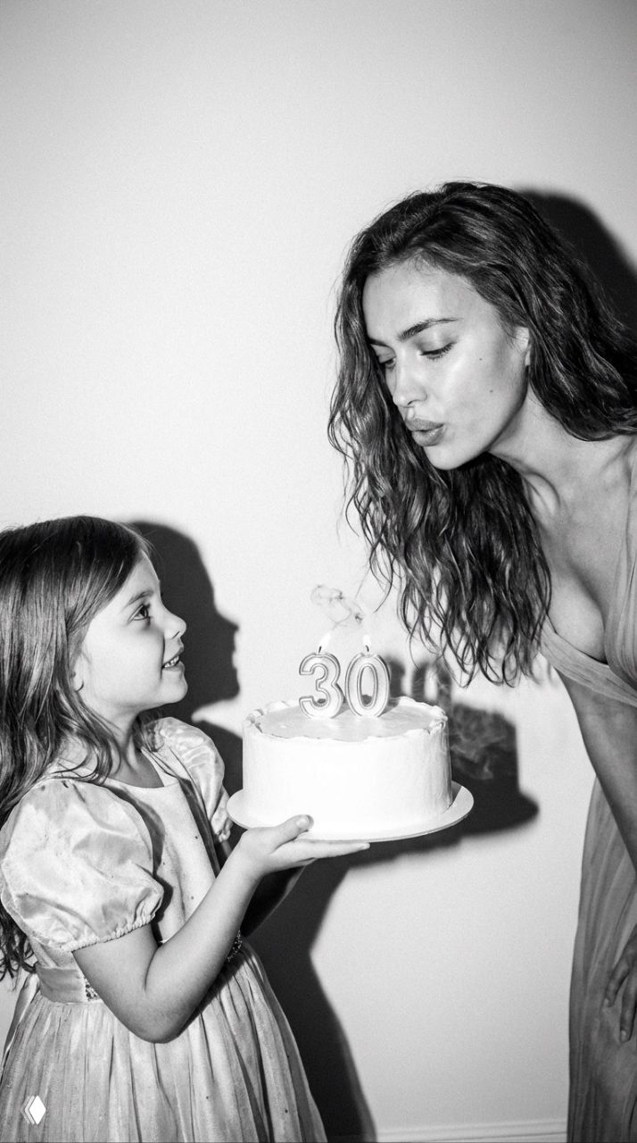 Чёрно‑белый вертикальный кадр 9:16: молодая женщина дует на свечи «30», девочка держит торт, резкий контраст и плёночная зернистость.