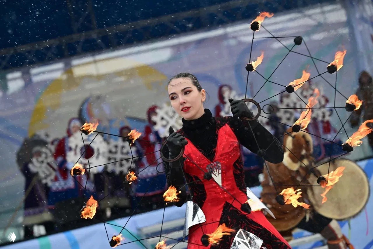 Артистка в сценическом костюме с горящими факелами исполняет огненное представление на открытой сцене во время северного фестиваля.