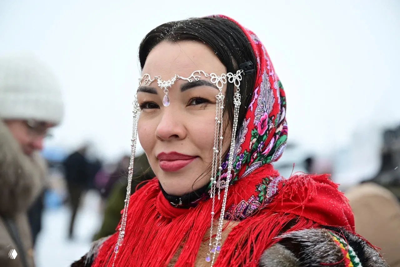 Портрет женщины в традиционном украшении на лбу и красном платке — крупный план лица на фоне зимней толпы и праздничной площадки.