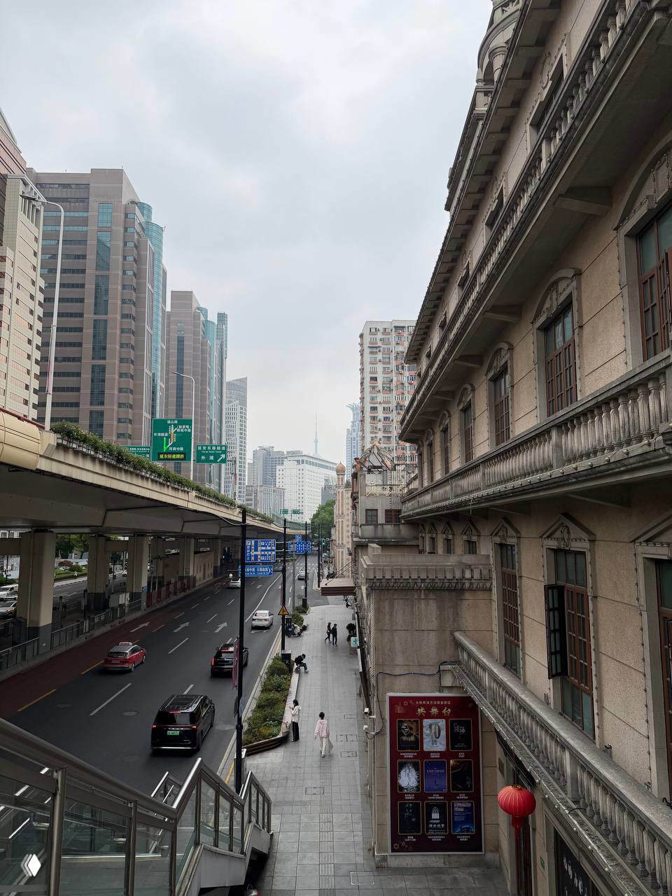 Уличный вид Шанхая с эстакадой и историческим фасадом, снято с перехода: городской пейзаж с машинами, пешеходами и приглушённым небом.