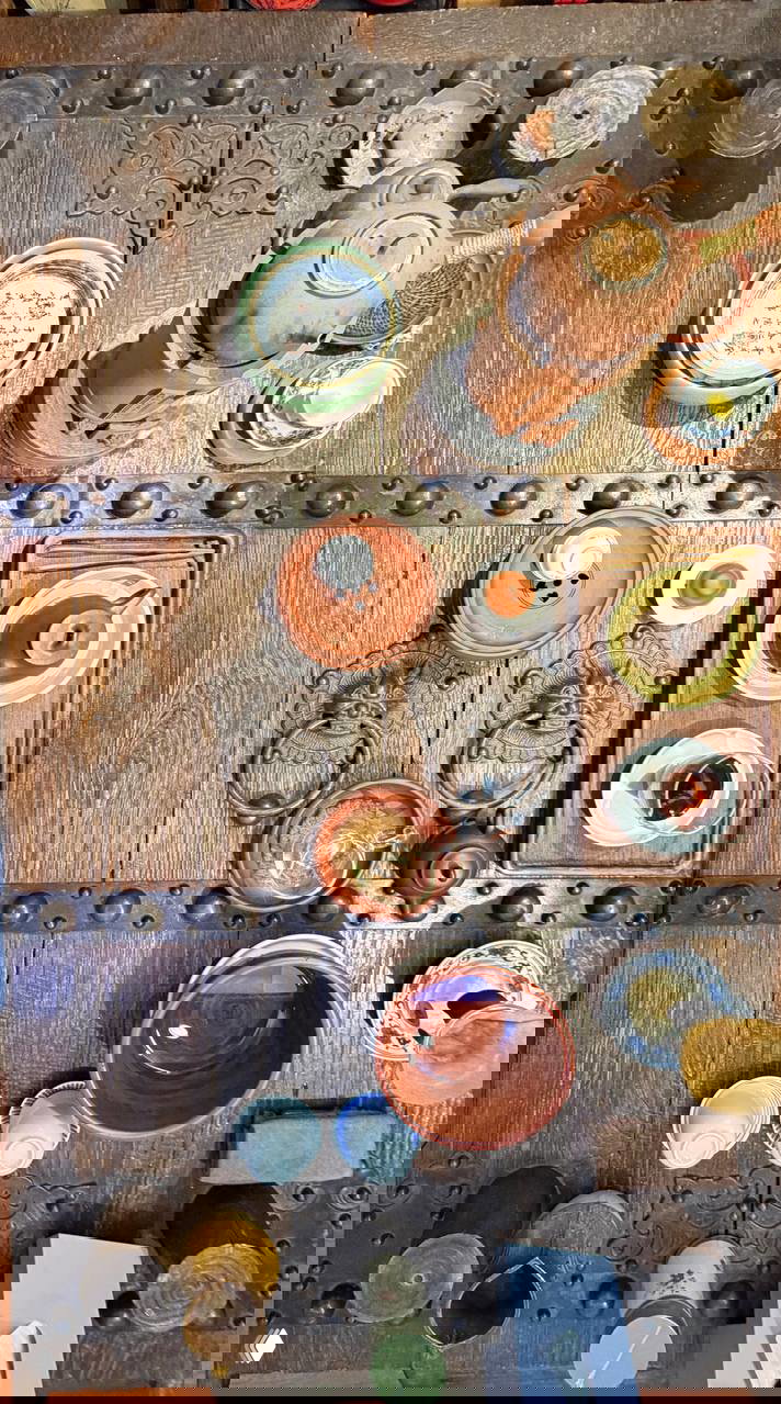 Вид сверху на чайные наборы: чайники, чашки и посуда, расставленные для дегустации на массивном деревянном столе с резными металлическими накладками.